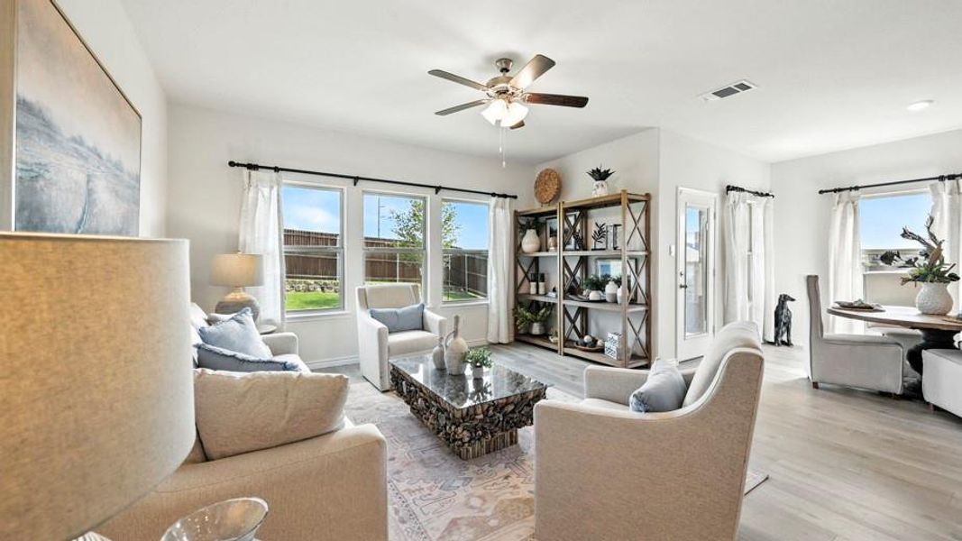 This open-concept living area features light-colored walls and flooring, a ceiling fan, and multiple windows providing natural light