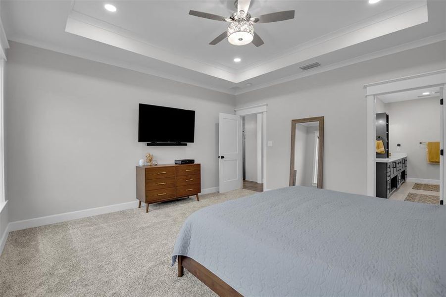 Carpeted bedroom featuring ceiling fan, a raised ceiling, crown molding, and connected bathroom