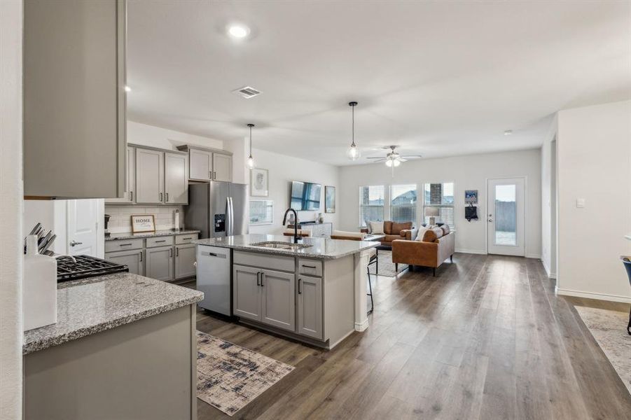 Kitchen with a center island with sink, stainless steel appliances, light stone countertops, pendant lighting, and sink