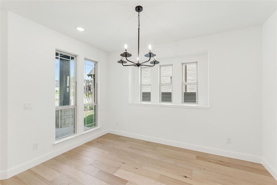 Empty dining room with light wood floors, black chandelier, and multiple windows Empty dining room with light wood floors, black chandelier, and multiple windows