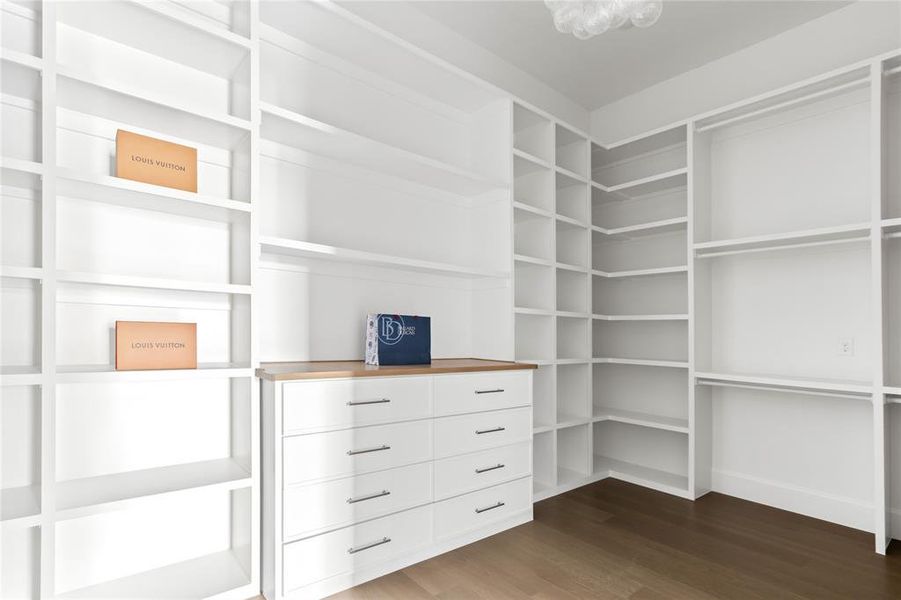 Custom-built closet featuring extensive shelving, hanging rods, an integrated dresser with a wood-finish countertop, and dark wood-finish flooring