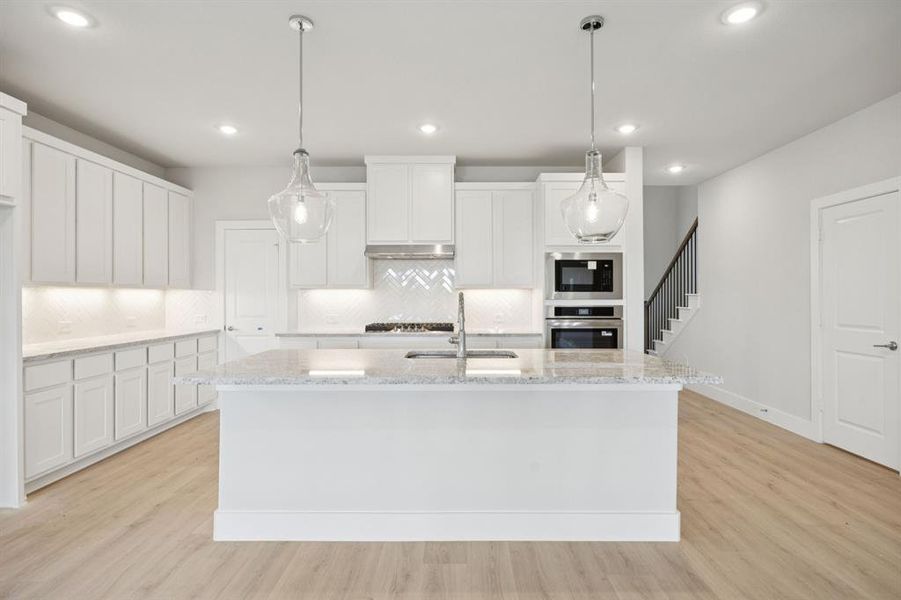 Kitchen featuring white cabinetry, decorative light fixtures, light stone counters, light wood-style flooring, and recessed lighting