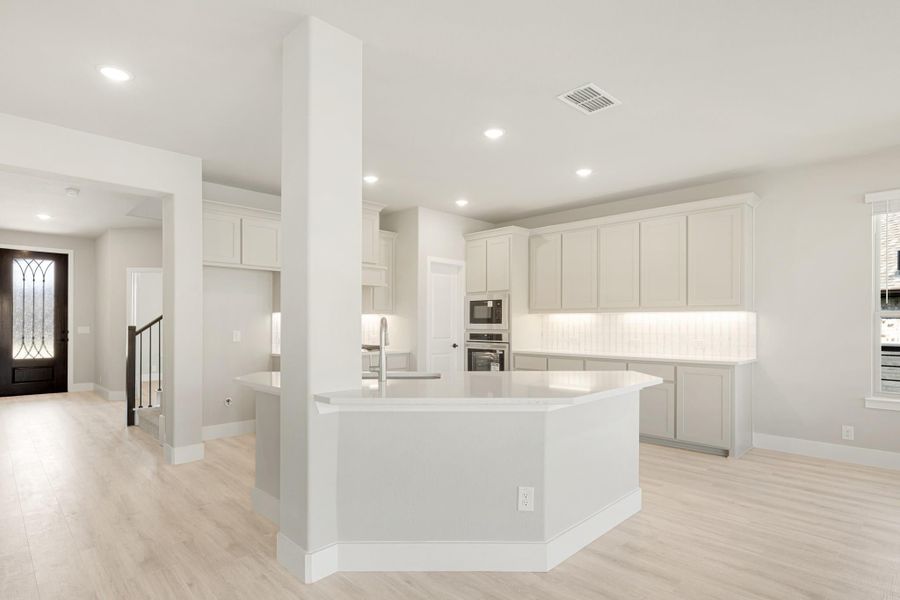 Open kitchen with large island, white upper cabinets, gray lower cabinets, subway tile backsplash, and light wood floors