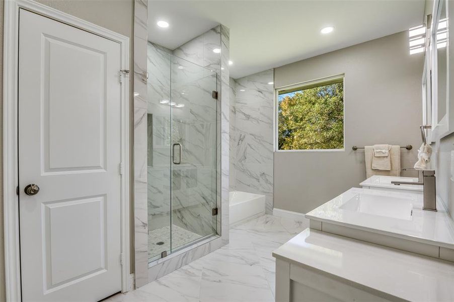 Bathroom featuring a bath, double vanity, light marble finish flooring, a marble finish shower, and recessed lighting