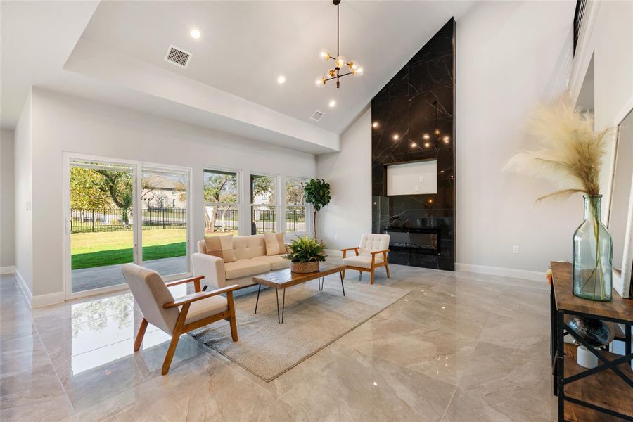 Living area featuring high vaulted ceiling, a chandelier, light marble finish flooring, and a fireplace
