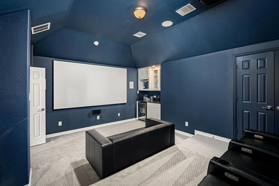 Home theater room featuring bar area, light colored carpet, wine cooler, and vaulted ceiling