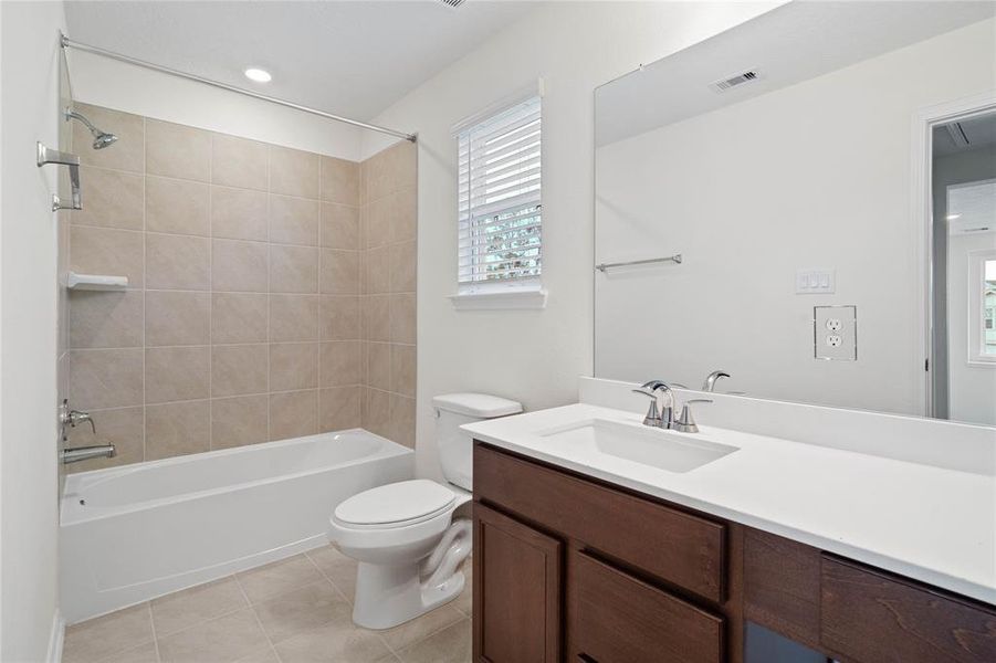 Secondary bath features tile flooring, bath/shower combo with tile surround, stained wood cabinets, beautiful light countertops, mirror, sleek fixtures and modern finishes.