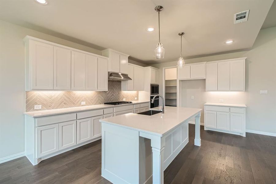 Kitchen with dark wood-type flooring, an island with sink, and white cabinets