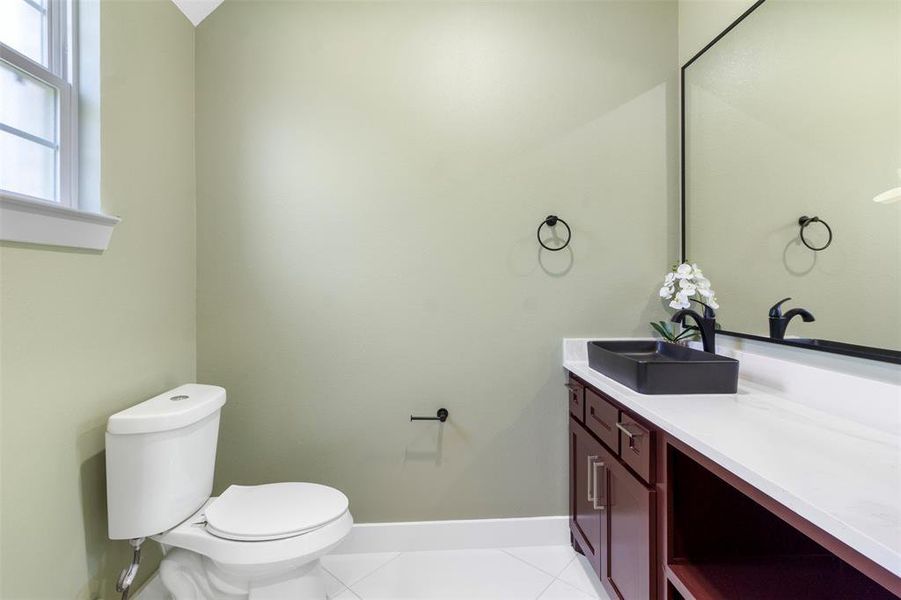 This bathroom features a modern design with a black sink and faucet, a large mirror, and a green accent wall. It includes a white toilet and a wooden vanity with ample counter space, creating a clean and stylish look.