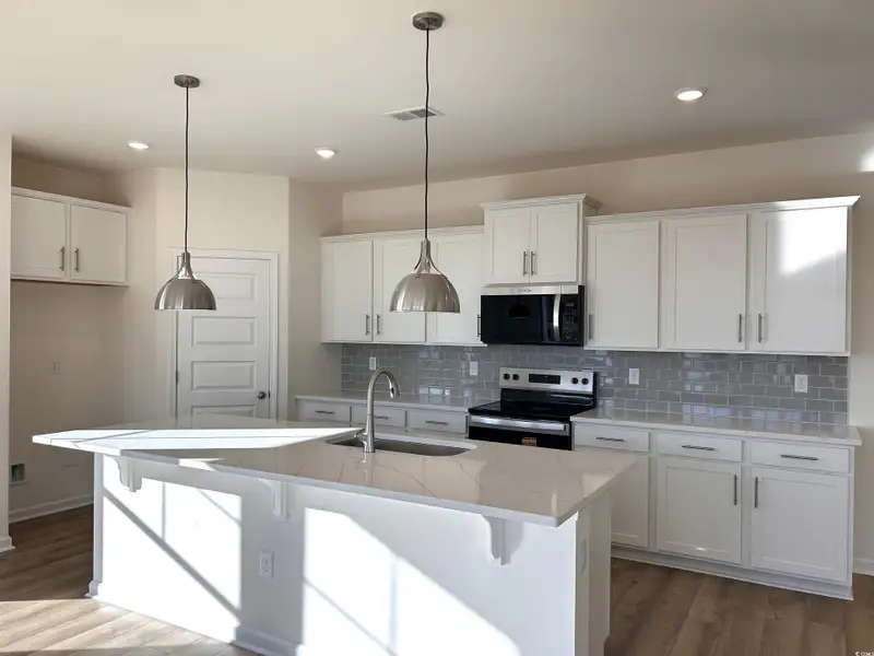 Kitchen featuring a breakfast bar, stainless steel appliances, white cabinets, an island with sink, and recessed lighting