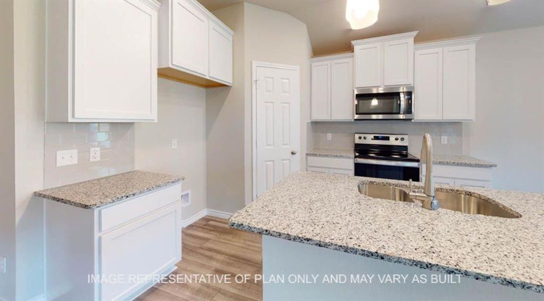 Kitchen with backsplash, white cabinets, stainless steel appliances, light wood finished floors, and light stone counters Kitchen with backsplash, white cabinets, stainless steel appliances, light wood finished floors, and light stone counters