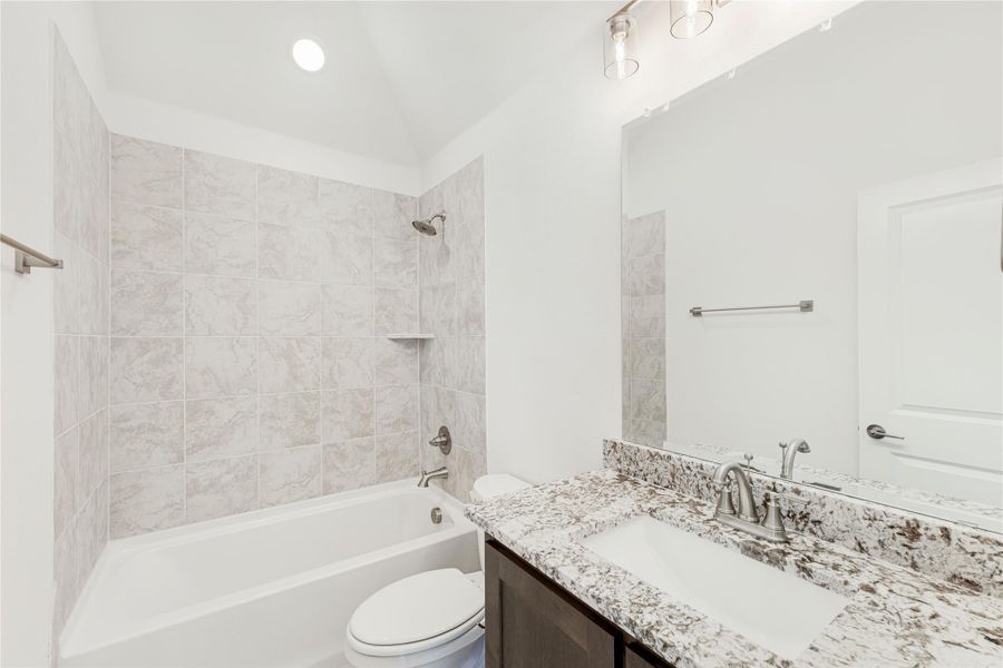 Bathroom with granite countertop vanity, tiled tub-shower combo, and white toilet Bathroom with granite countertop vanity, tiled tub-shower combo, and white toilet