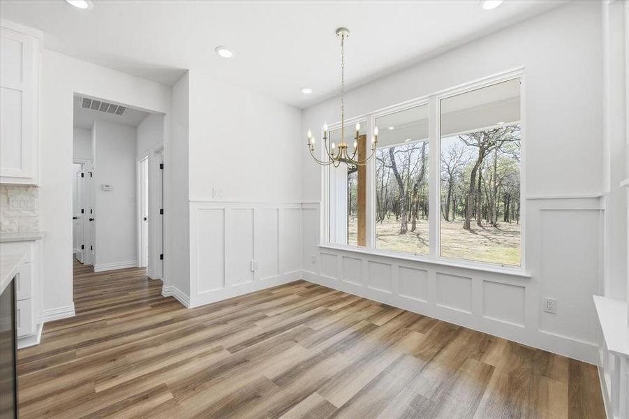 Unfurnished dining area with hanging lights, wainscoting, light wood-style flooring, a decorative wall, and wine cooler