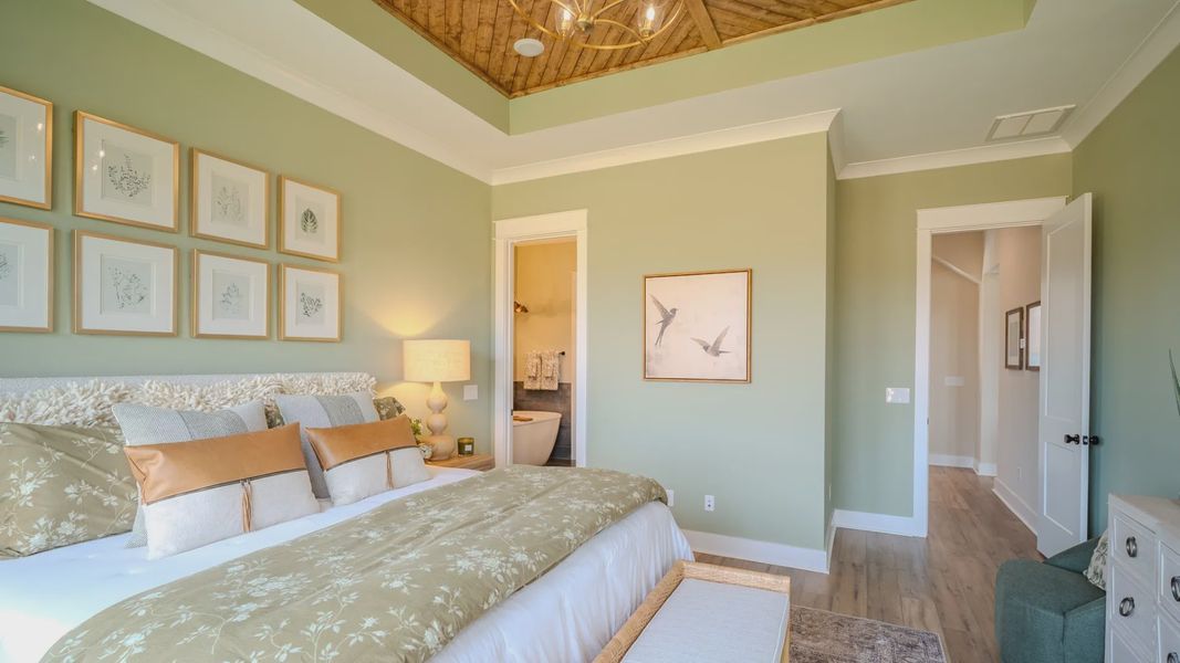 Spacious primary suite with tray ceiling, hard surface flooring, and access to primary bathroom Spacious primary suite with tray ceiling, hard surface flooring, and access to primary bathroom