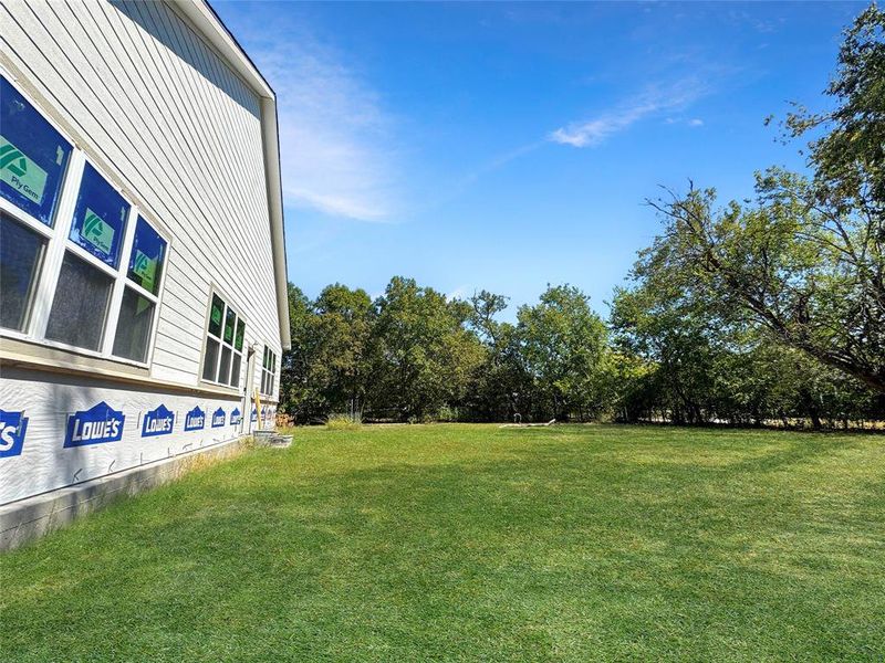 View of grassy yard featuring view of wooded area View of grassy yard featuring view of wooded area