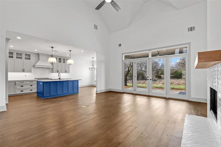 Unfurnished living room with dark wood-type flooring, sink, high vaulted ceiling, a fireplace, and ceiling fan with notable chandelier