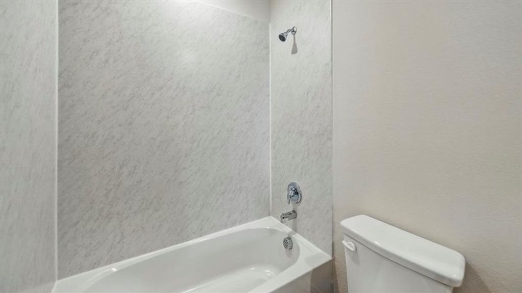 White bathtub with integrated shower, chrome fixtures, and a light-toned, textured surround