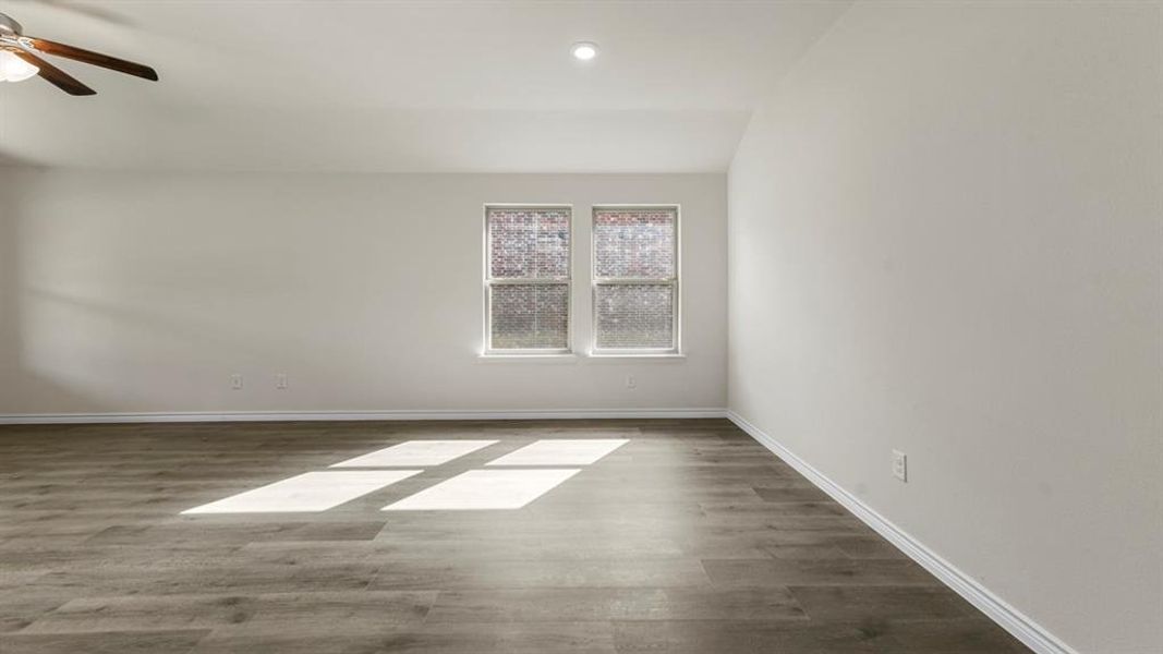 Spacious room featuring wood-finish flooring, light-colored walls, and a ceiling fan with integrated lighting