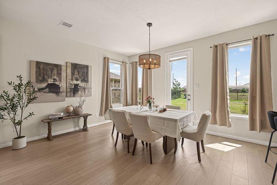 Sunlit dining area showcases upgraded light wood floors, oversized windows, and a modern statement chandelier.