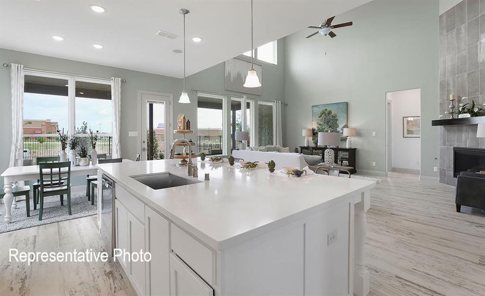 Kitchen featuring a fireplace, an island with sink, white cabinets, sink, and pendant lighting