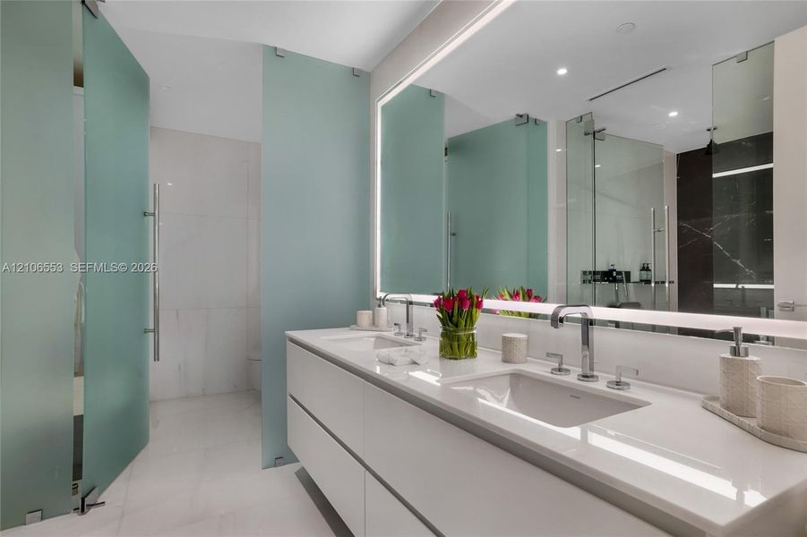 Floating dual-sink vanity with a solid surface countertop, integrated LED-backlit mirror, and frosted glass privacy partitions