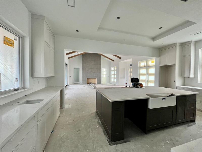 Kitchen featuring light stone counters, a raised ceiling, a tile fireplace, a center island, and white cabinetry