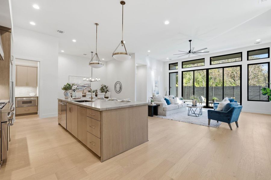 Kitchen with pendant lighting, light wood finished floors, open floor plan, light stone countertops, and a ceiling fan