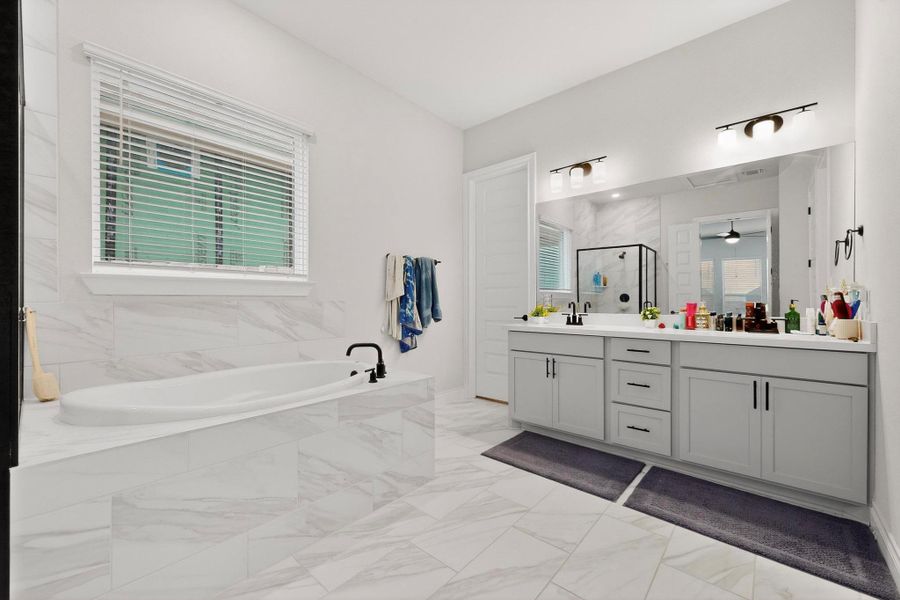 Bathroom featuring a stall shower, double vanity, light marble finish flooring, a bath, and plenty of natural light