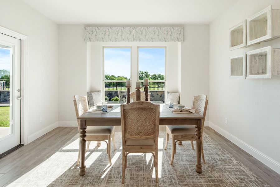 Bright dining room with wooden table, six chairs, hardwood floors, and large windows overlooking a backyard.