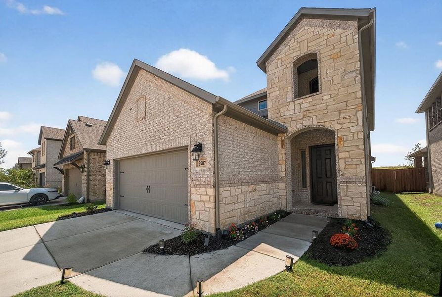 Stone and brick exterior featuring an arched entryway, integrated garage, and landscaped front planting beds