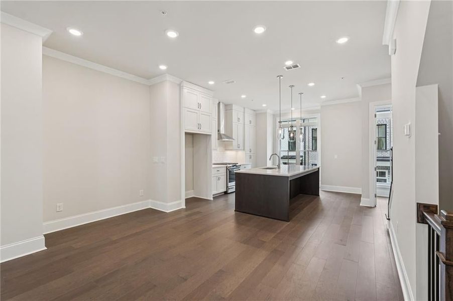 Dual tone kitchen with crown molding, gas stove, dark wood finished floors, decorative light fixtures, and a kitchen island with sink