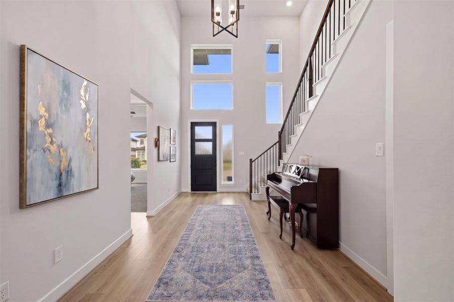 A grand 8-foot entry door with elegant rain glass and a coordinating sidelight creates a sophisticated arrival. Two dramatic picture windows above the entry extend toward the soaring 20-foot ceiling, flooding the two-story foyer with natural light and enhancing the impressive sense of scale. This photo has been virtually staged.