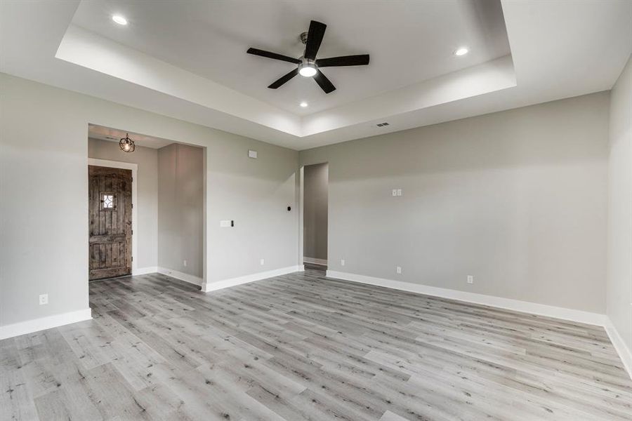 Unfurnished room with light hardwood / wood-style floors, a raised ceiling, and ceiling fan