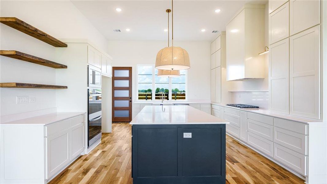 Kitchen with light wood-type flooring, hanging light fixtures, a center island, white cabinetry, and appliances with stainless steel finishes