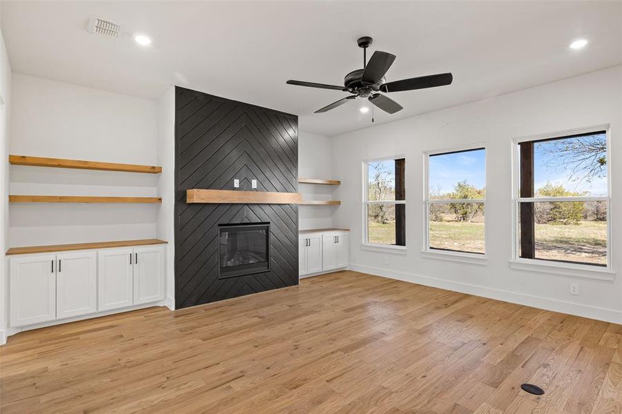 Unfurnished living room featuring a large fireplace, ceiling fan, and light hardwood / wood-style floors