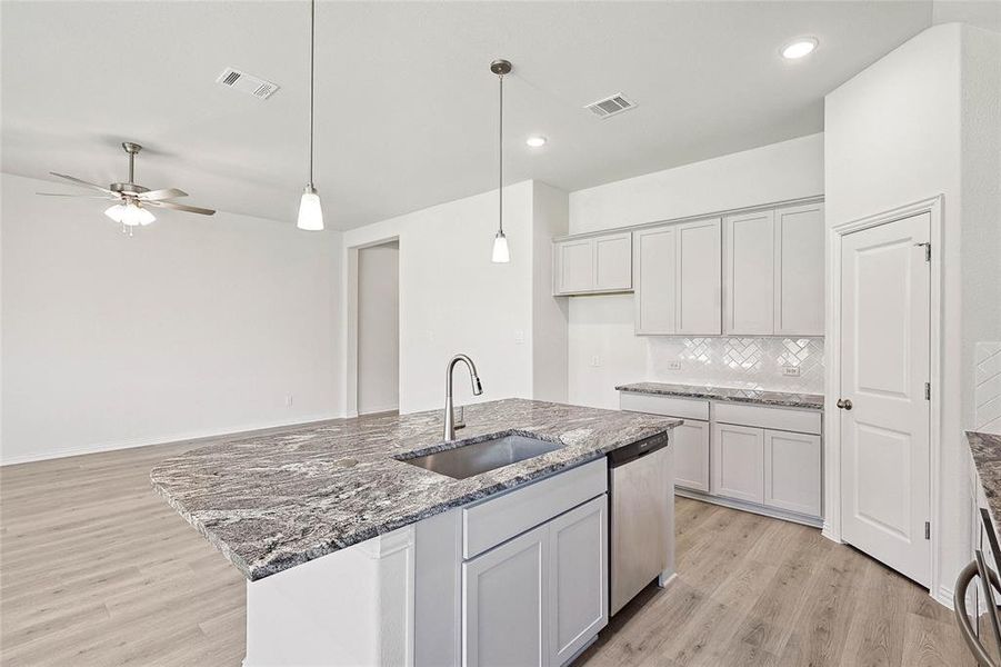 Kitchen featuring stainless steel dishwasher, an island with sink, backsplash, ceiling fan, and sink