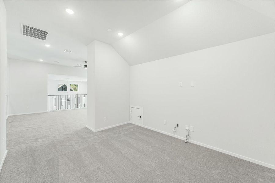 Empty upstairs bonus room with vaulted ceiling, gray carpet, and open railing overlooking lower level Empty upstairs bonus room with vaulted ceiling, gray carpet, and open railing overlooking lower level