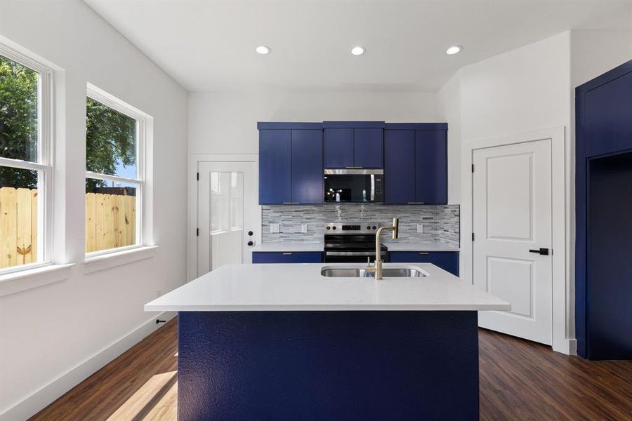 Kitchen with blue cabinetry, a center island with sink, stainless steel appliances, light stone countertops, and dark wood finished floors