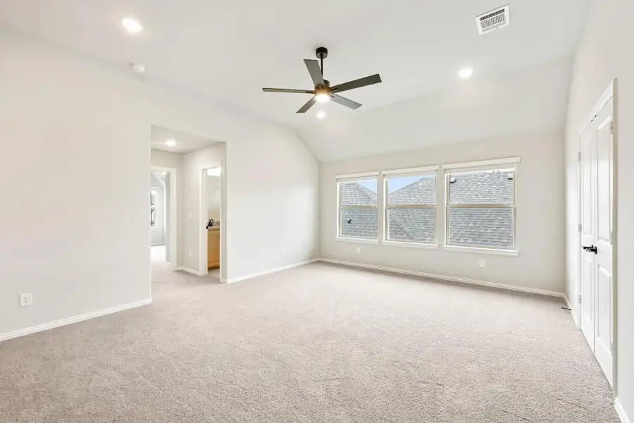 Spacious bedroom with vaulted ceiling, ceiling fan, carpet flooring, and ensuite bathroom doorway Spacious bedroom with vaulted ceiling, ceiling fan, carpet flooring, and ensuite bathroom doorway