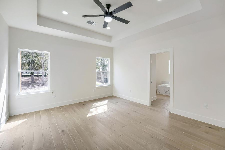 Recessed lighting illuminates this bright bedroom, featuring light wood flooring and a modern ceiling fan.