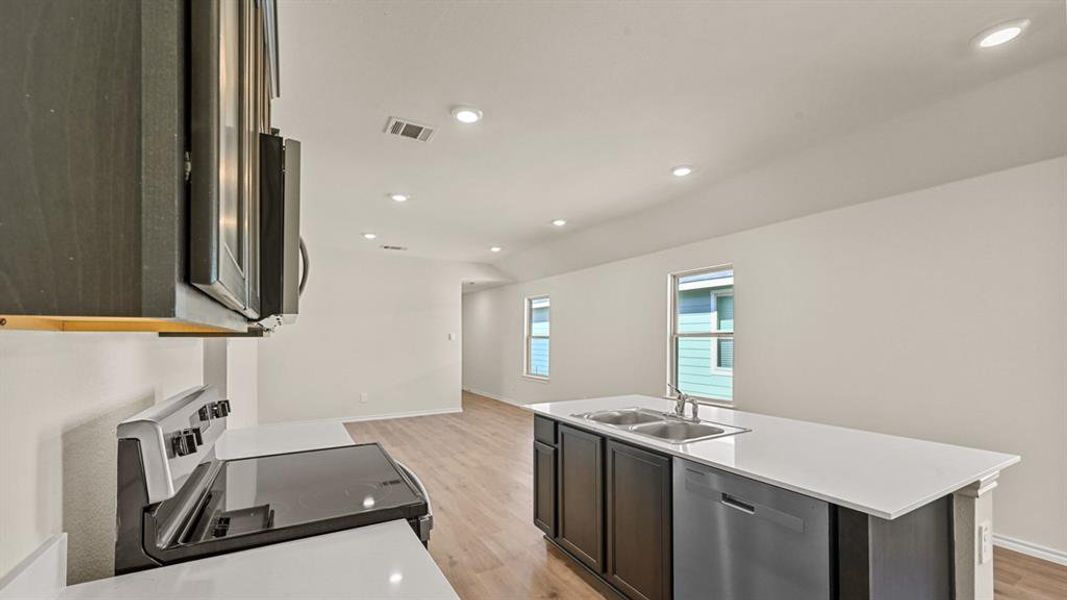 Kitchen featuring an island with dual basin sink and stainless steel dishwasher, white countertops, built-in microwave, and wood-finish flooring