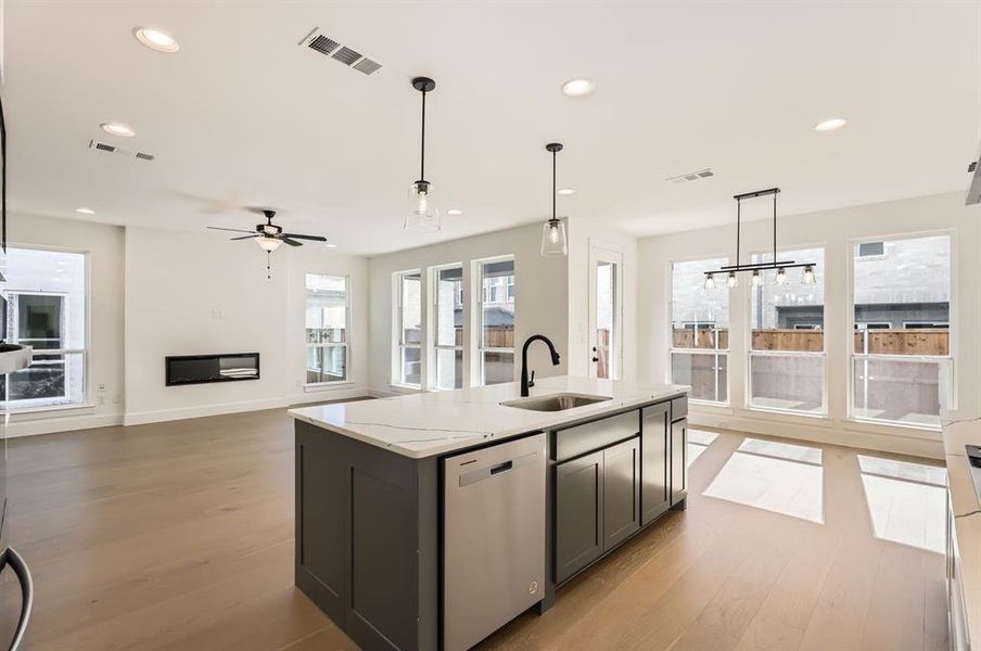 Kitchen featuring sink, light stone countertops, stainless steel dishwasher, light hardwood / wood-style flooring, and pendant lighting