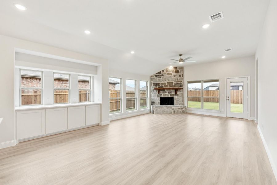 Open living room with stone fireplace, light wood floors, ceiling fan, and large windows
