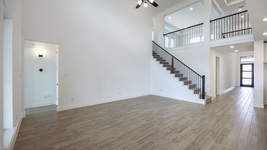 Unfurnished living room featuring a towering ceiling, light wood-style floors, recessed lighting, and stairway Unfurnished living room featuring a towering ceiling, light wood-style floors, recessed lighting, and stairway