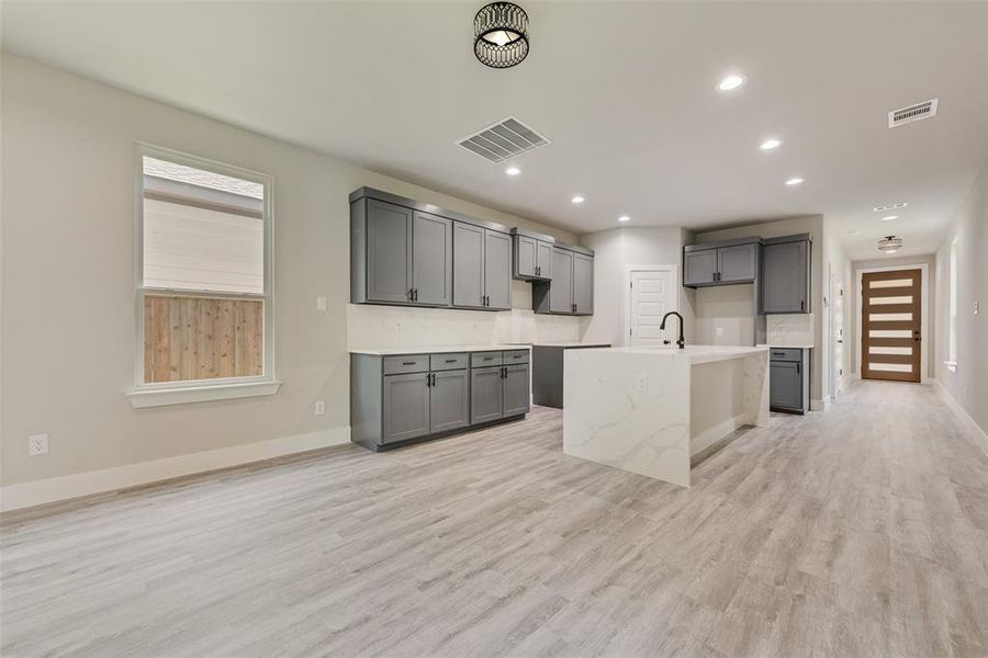 Kitchen with gray cabinets, light wood-style floors, recessed lighting, and a center island with sink Kitchen with gray cabinets, light wood-style floors, recessed lighting, and a center island with sink
