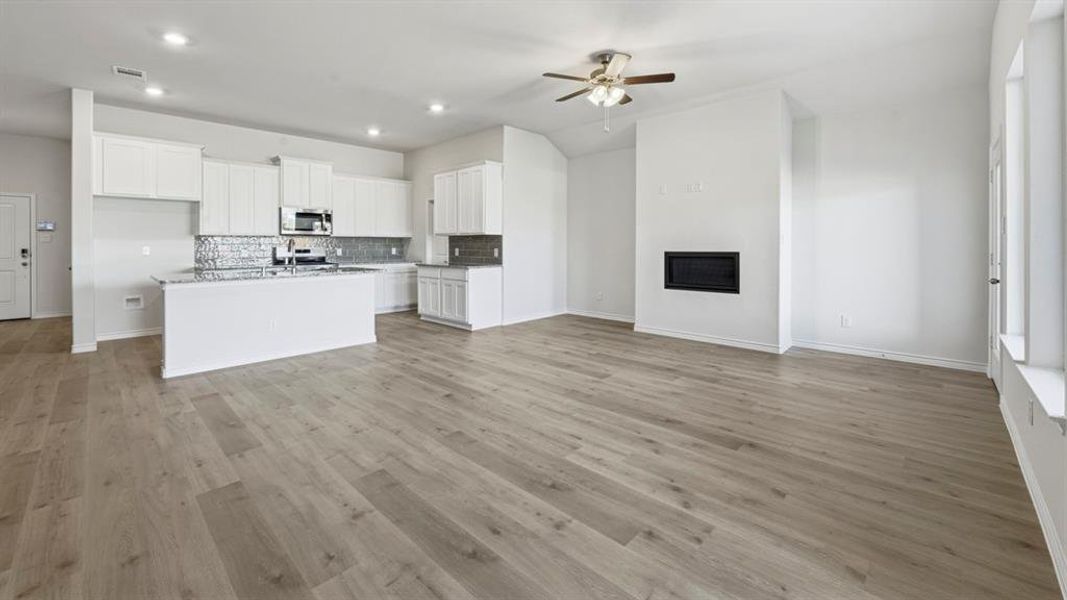 Kitchen with open floor plan, white cabinets, a glass covered fireplace, an island with sink, and light wood finished floors