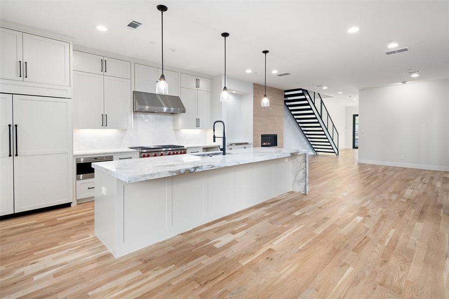 Kitchen with light stone countertops, pendant lighting, a center island with sink, white cabinets, and exhaust hood