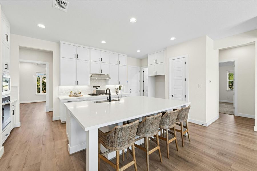 Kitchen with a kitchen bar, white cabinets, light wood-type flooring, recessed lighting, and a large island with sink Kitchen with a kitchen bar, white cabinets, light wood-type flooring, recessed lighting, and a large island with sink