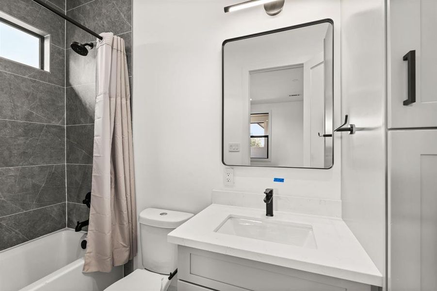 Secondary bathroom offers a quartz countertop, modern mirror, built-in cabinetry and tub/shower combo.