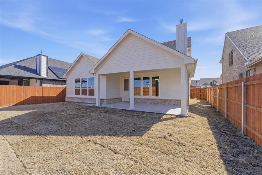 Rear view of property featuring a patio area, a fenced backyard, a chimney, and stone siding